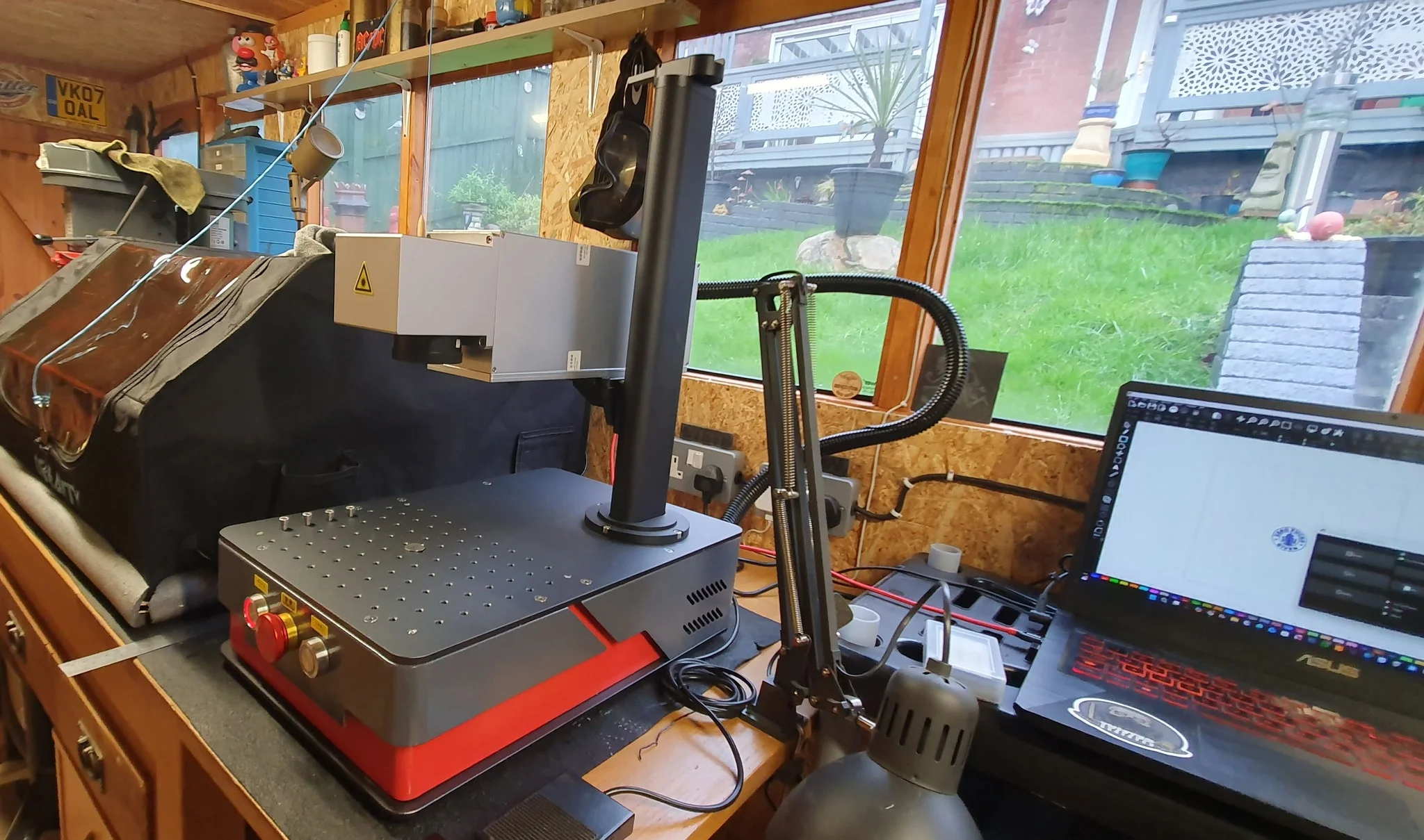 Haotian 50W M8 compact fiber laser set up in home workshop with laptop running EZCad software