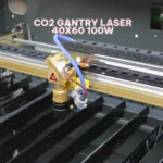 Gold-plated laser head and lens assembly on the gantry of a 100W CO2 cutting machine.