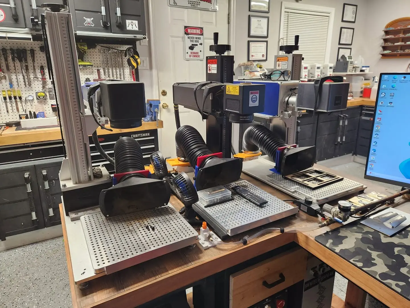 Three Haotian fiber lasers with fume extractor hoods on a customer garage workbench