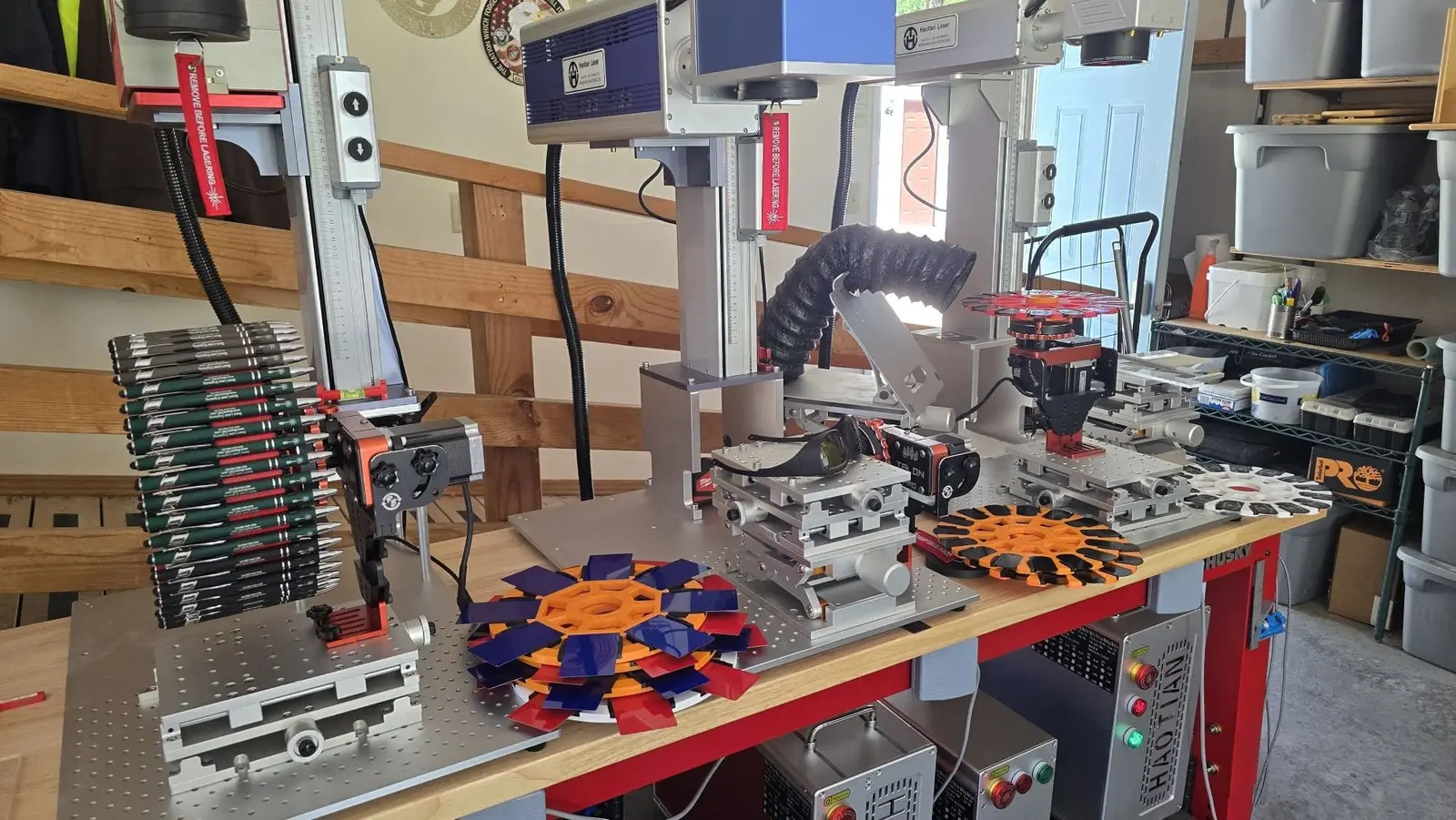 Customer garage setup with three Haotian fiber lasers engraving promotional pens on disc feeders